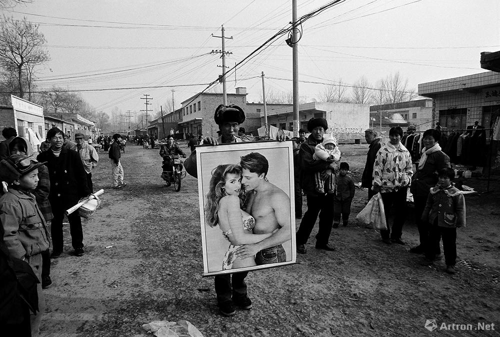 春节前的年货市场上，一位小贩在向行人展示新潮年画